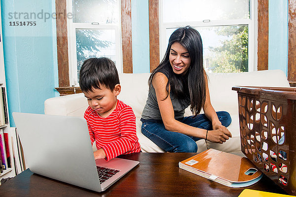 Männliches Kleinkind mit Mutter  die zu Hause am Laptop tippt