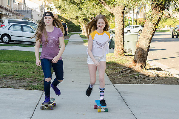 Zwei jugendliche Skateboardfahrer-Schwestern skateboarden auf dem Bürgersteig