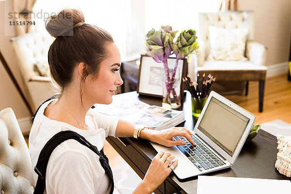 Weibliche Mode- und Lifestyle-Bloggerin tippt am Schreibtisch am Laptop