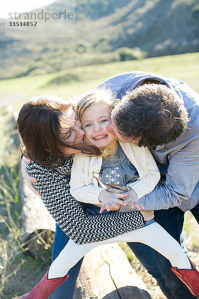 Mittelgroßes erwachsenes Paar küsst Tochter auf dem Feld auf die Wangen