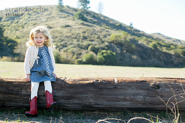Porträt eines auf einem Baumstamm sitzenden Mädchens in roten Cowboy-Stiefeln