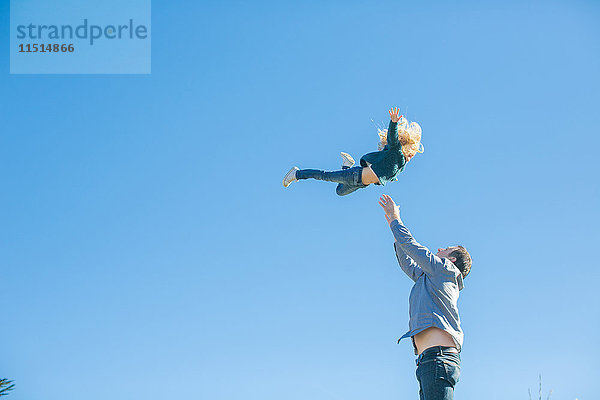 Mädchen wird vom Vater gegen blauen Himmel in die Luft geschleudert