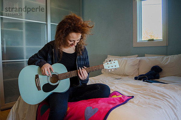 Teenager spielt Gitarre im Schlafzimmer