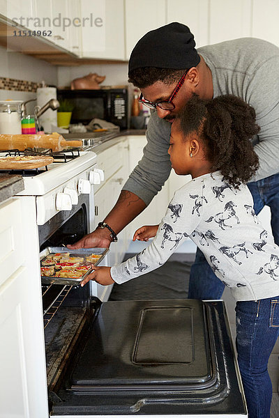 Vater und Tochter schieben ungebackene Kekse in den Ofen