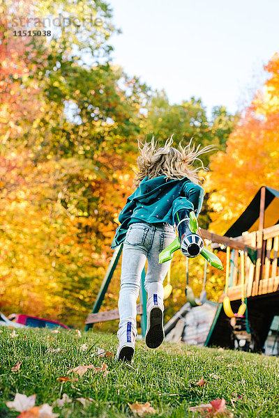 Rückansicht eines Mädchens  das mit einer Spielzeugrakete im Garten rennt