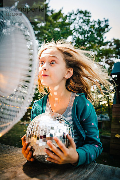 Mädchen zieht Gesicht vor windigem Elektroventilator am Gartentisch