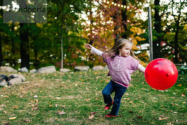 Mädchen spielt mit rotem Luftballon im Garten