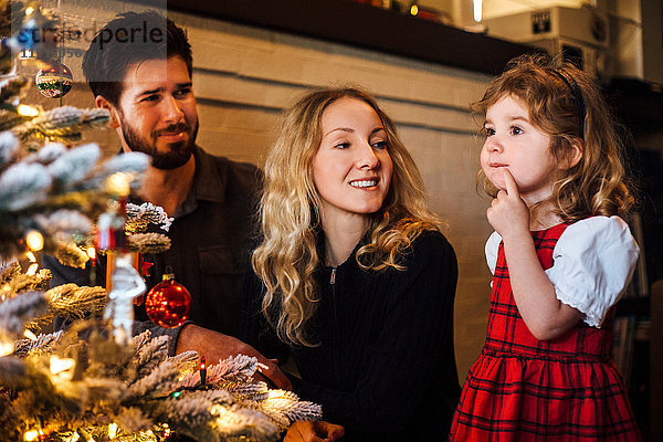 Weibliches Kleinkind mit Eltern  die auf den Weihnachtsbaum starren