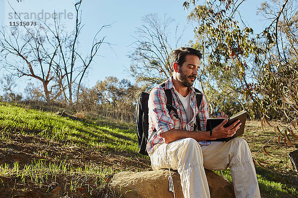Mittelgroßer erwachsener Mann wandert  sitzt auf einem Felsblock und liest Buch