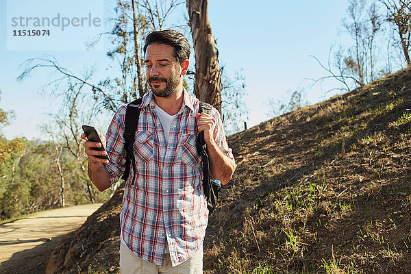 Mittelgroßer erwachsener Mann beim Wandern  Blick auf Smartphone