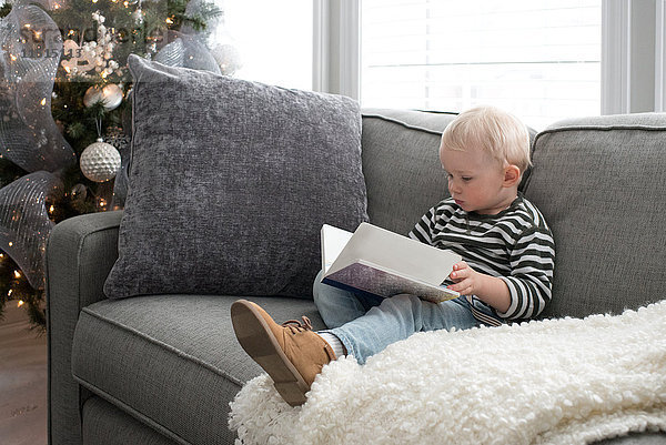 Junge sitzt auf dem Sofa und schaut sich das Buch an.