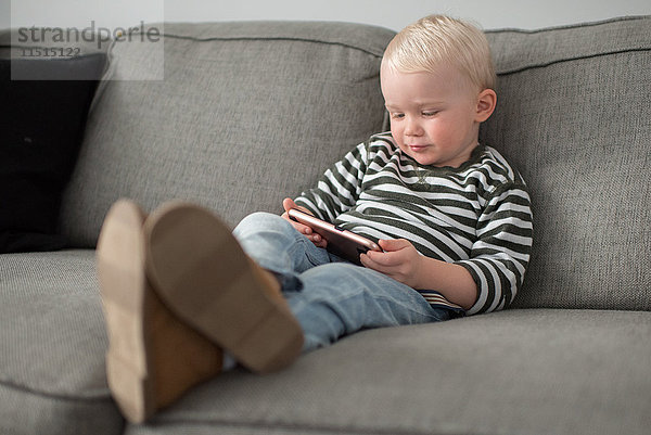 Junge sitzt auf dem Sofa und schaut auf ein Smartphone