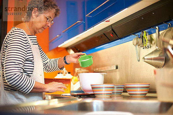 Ältere Frau in der Küche  misst Zutaten in Rührschüssel