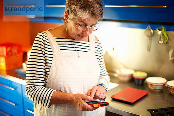 Ältere Frau in der Küche  die ein Smartphone benutzt