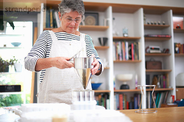 Ältere Frau benutzt Pfannkuchentrichter  um Mischung in Plastiktöpfe zu gießen