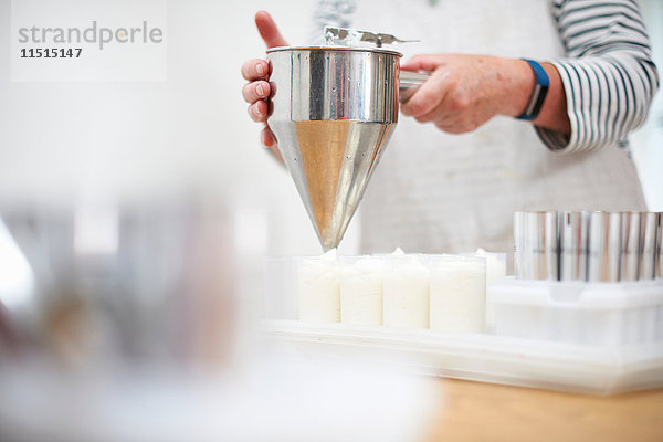 Ältere Frau in der Küche  die mit dem Pfannkuchentrichter Sahne und selbstgemachte Kosmetika in Töpfe abgibt  Mittelteil