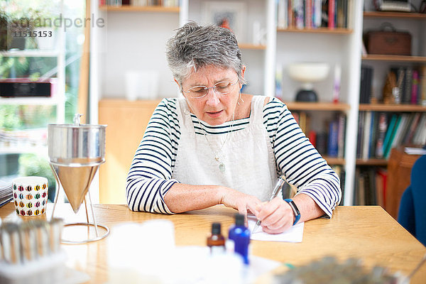Ältere Frau sitzt am Küchentisch und schreibt auf einem Notizblock