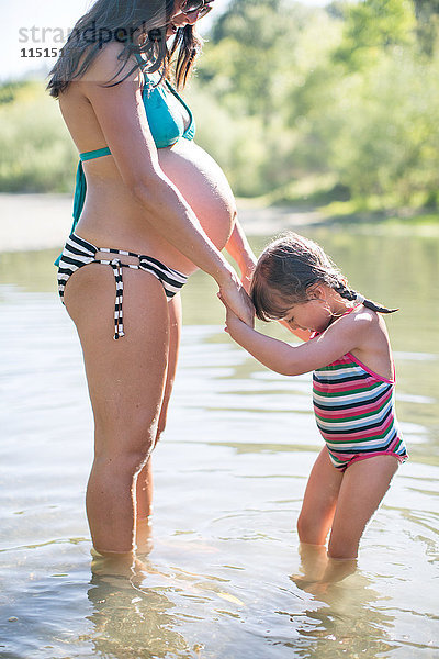 Schwangere Mutter und Tochter stehen im See und halten sich an den Händen