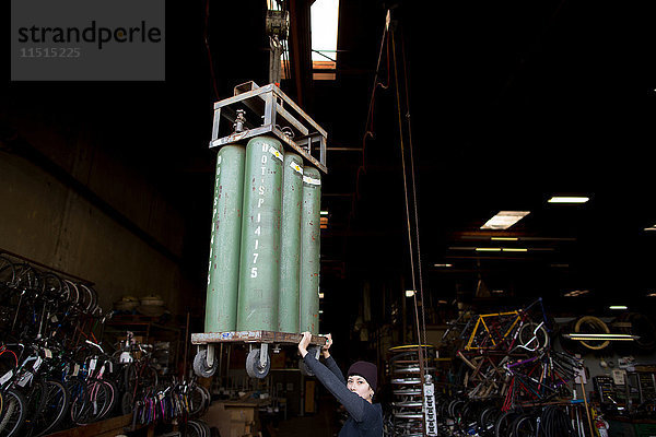 Porträt einer Metallschmiedin  die in einer Werkstatt einen Kettenzug stabilisiert