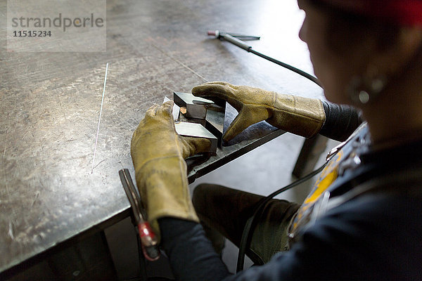 Über-Schulter-Ansicht einer Metallschmiedin beim Ausrichten von Metall an der Werkbank