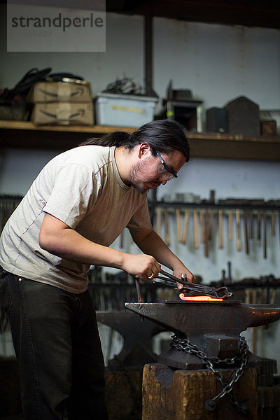 Männlicher Metallschmied beim Formen von rotglühendem Metall auf Werkstattamboss