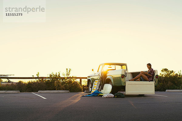 Junge Surferin betrachtet ein Smartphone auf dem Rücksitz eines Pickup-Trucks in Newport Beach  Kalifornien  USA