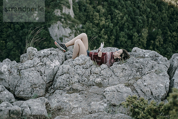 Kaukasische Frau liegt auf einem Bergfelsen und liest eine Zeitschrift