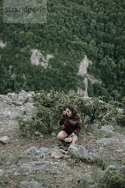 Lächelnde kaukasische Frau hockt auf einem Berg und hält eine Pfanne