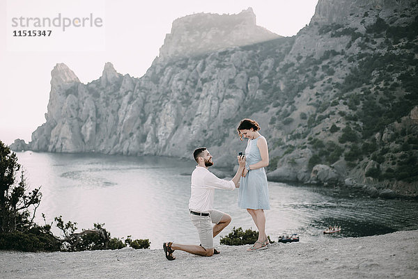 Kaukasischer Mann macht einer Frau am Strand einen Heiratsantrag