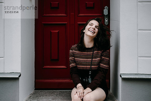 Lachende kaukasische Frau  die in der Tür sitzt