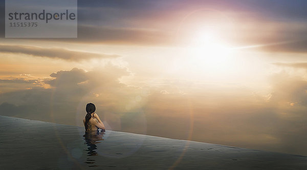 Chinesische Frau im Infinity-Pool bewundert den Sonnenuntergang
