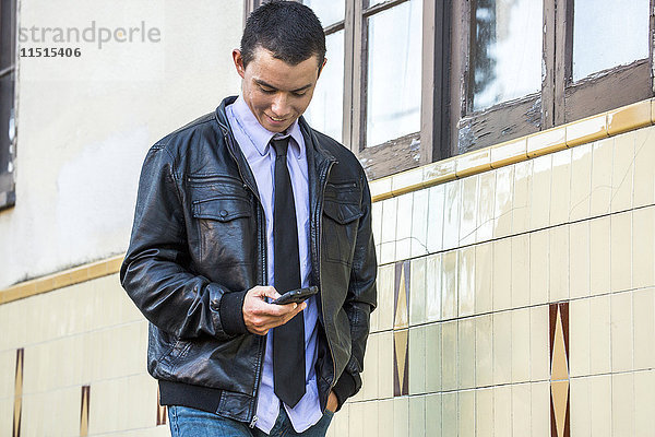 Gemischtrassiger Mann mit Lederjacke  der eine SMS auf seinem Handy schreibt