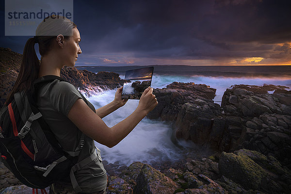 Kaukasische Frau fotografiert Sonnenuntergang am Meer mit digitalem Tablet