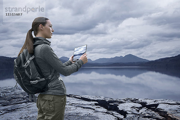 Kaukasische Frau fotografiert Bergsee mit digitalem Tablet