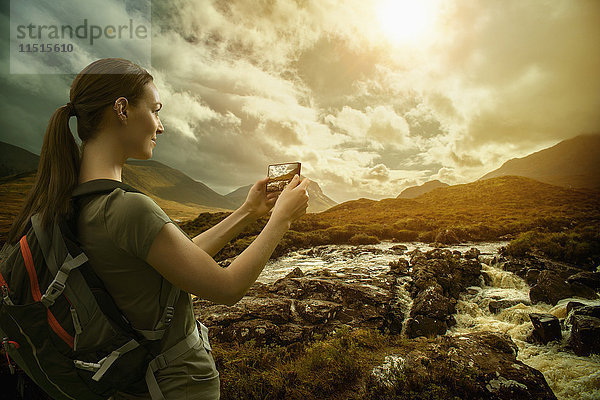 Kaukasische Frau fotografiert Bergfluss mit Mobiltelefon