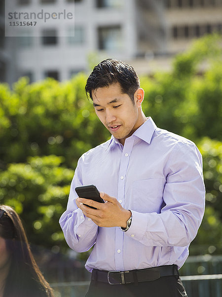 Chinesischer Geschäftsmann schreibt im Freien eine SMS mit seinem Handy