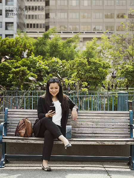 Chinesische Geschäftsfrau  die auf einer Bank in der Stadt mit ihrem Handy telefoniert
