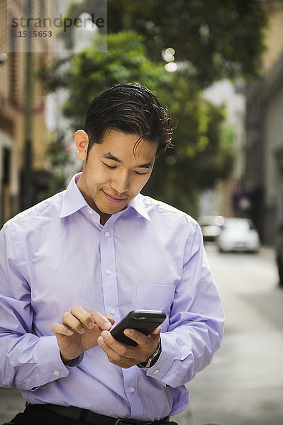 Chinesischer Geschäftsmann  der in der Stadt eine SMS auf seinem Mobiltelefon schreibt