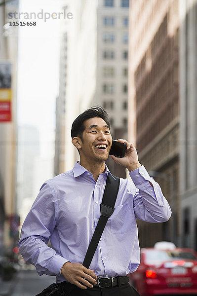 Chinesischer Geschäftsmann  der in der Stadt mit einem Handy telefoniert