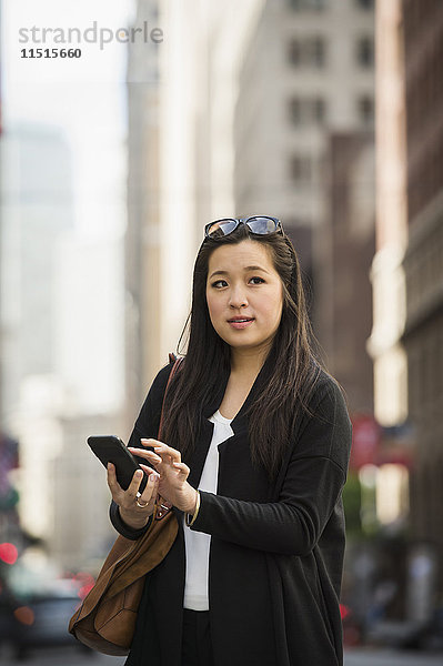 Chinesische Geschäftsfrau  die in der Stadt eine SMS mit ihrem Handy schreibt