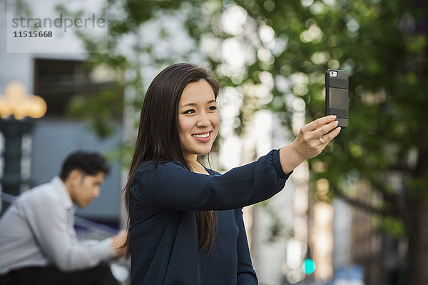 Chinesische Geschäftsfrau posiert für Handy-Selfie im Freien