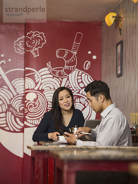 Chinesische Geschäftsleute  die im Restaurant mit ihrem Handy telefonieren
