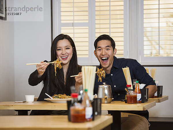 Lächelndes chinesisches Paar hält Nudeln mit Stäbchen in einem Restaurant