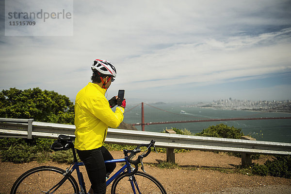 Hispanoamerikanischer Mann auf dem Fahrrad  der mit seinem Mobiltelefon das Hafenviertel fotografiert