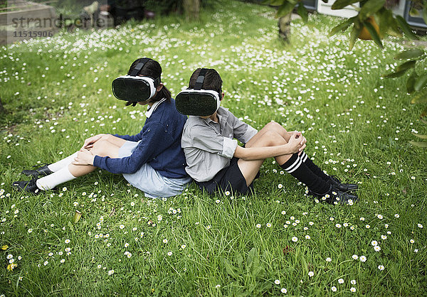 Mixed-Race-Bruder und -Schwester sitzen im Gras und tragen Virtual-Reality-Brillen