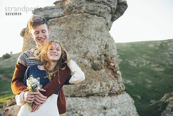 Kaukasisches Paar umarmt in der Nähe von Felsen mit Blumenstrauß