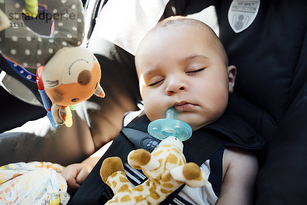 Gemischtrassiger Babyjunge mit Schnuller im Autositz schlafend