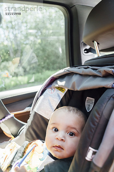 Porträt eines neugierigen gemischtrassigen kleinen Jungen im Autositz