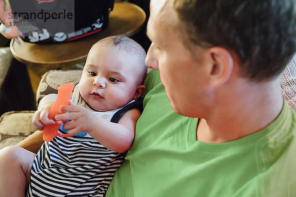 Vater hält Baby  das mit Spielzeug spielt