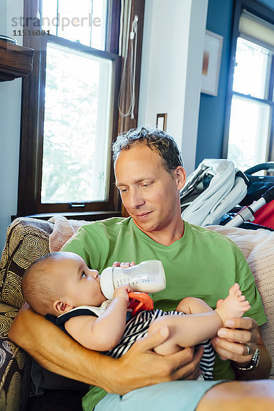 Vater hält seinen kleinen Sohn und trinkt Milch aus der Flasche